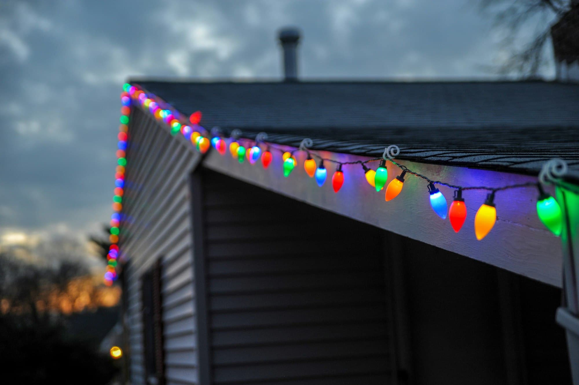 Multi-coloured holiday bulbs clipped along a roof edge at dusk
