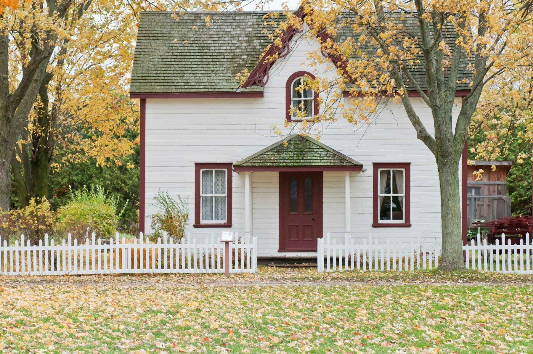 White house with a picket fence under autumn maple trees