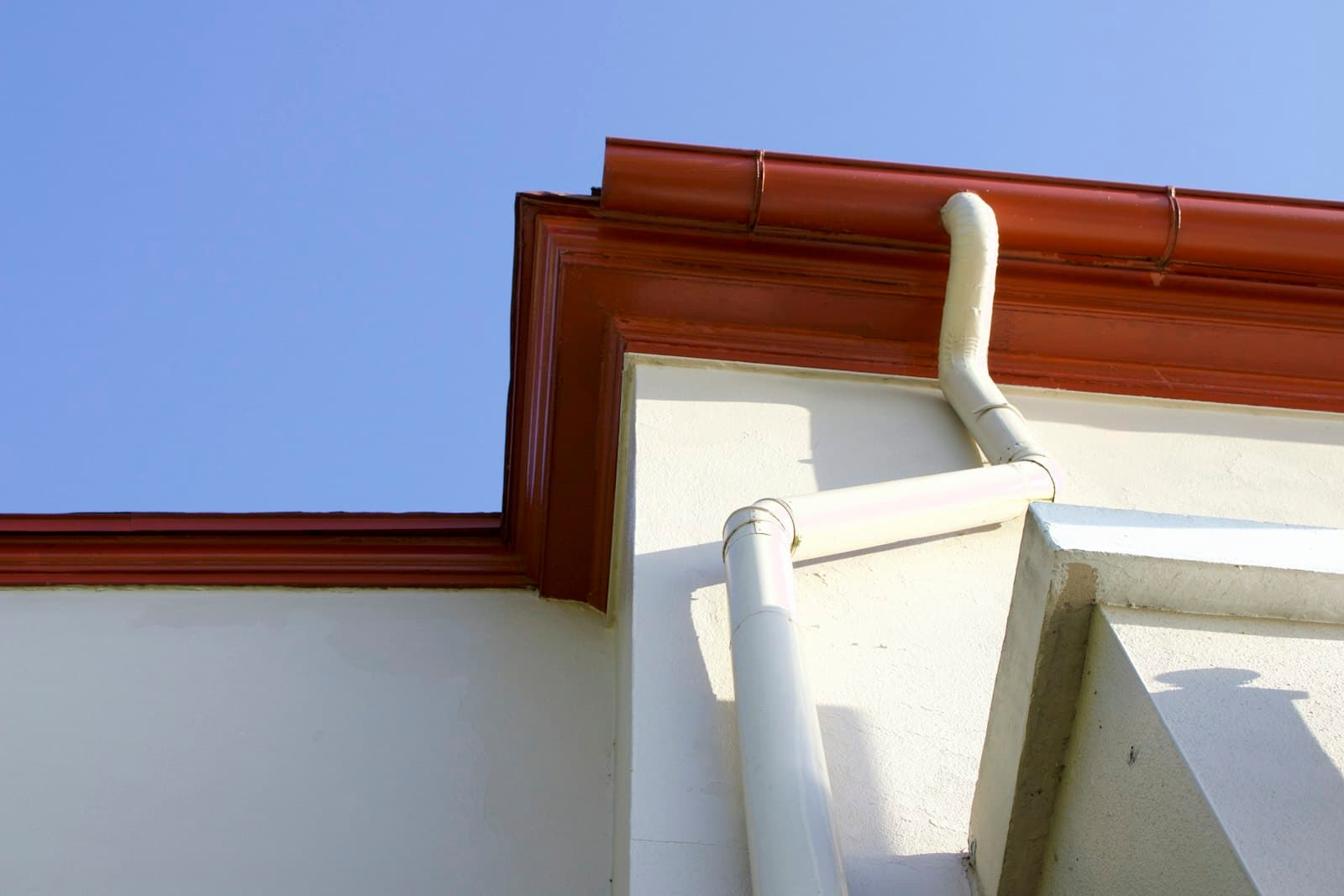 Clean white gutter and downspout under a blue sky